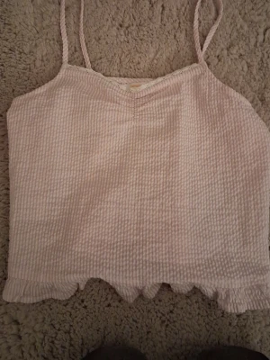 Ljusrosa linnetopp med volangkant - Supersöt ljusrosa linnetopp med tunna axelband och volangkant nedtill. Toppen har en ribbad struktur och är perfekt för varma dagar. Passar dig som gillar en feminin och enkel stil.