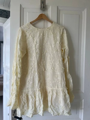 Ljusgul klänning NA-KD - Ljusgul kort klänning med långa ärmar och blommor från NA-KD, även ganska öppen i ryggen.💛 Storlek 38 och normal i storleken. Endast använd 2 gånger. Bara att skriva vid frågor eller för fler bilder💛