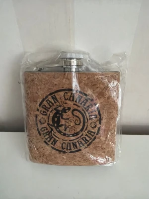 Plunta med kork och Gran Canaria-tryck - Säljer en plunta med korkbeklädd framsida och svart tryck med texten 'Gran Canaria' och en ödla i mitten. Pluntan har metallock och är perfekt som souvenir eller present. Unik design som sticker ut i samlingen.