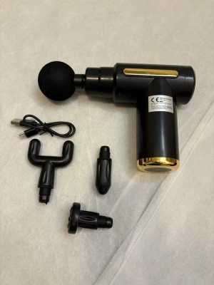 Svart massagepistol med tillbehör - Massagepistol i svart med gulddetaljer, levereras med fyra olika massagehuvuden och USB-laddkabel. Perfekt för återhämtning och muskelavslappning. Kommer i originalförpackning med instruktioner.