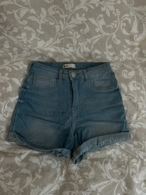 Högmidjade blå jeansshorts - Säljer ett par klassiska högmidjade jeansshorts från H&M i ljusblå denim.