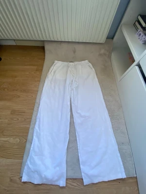 Vita vida linnebyxor med dragsko - Säljer ett par vita linnebyxor med avslappnad passform och dragsko i midjan. Byxorna har raka, vida ben och är tillverkade i ett lätt och luftigt linnematerial. Perfekta för en chill och stilren look. köpta på gina tricot.