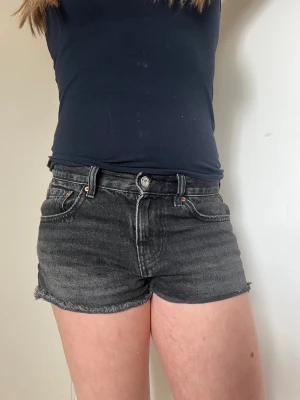 Svarta jeansshorts  - Säljer ett par svarta jeansshorts från Gina med klassisk femficksmodell och rå, fransig kant nedtill. Shortsen har medelhög midja, knappgylf och bälteshällor. Perfekta till sommaren för en avslappnad och trendig look.
