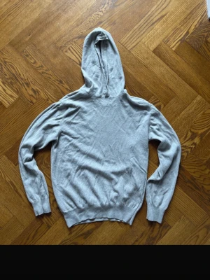 Pascal hoodie oscar Jacobsson   - Snygg beige hoodie från oscar Jacobsson klassisk huva och ribbade muddar vid ärmslut och nederkant. Tillverkad i Italien och har en mjuk, tunn stickad känsla som passar perfekt till vardagslooken. Enkel och stilren design utan tryck eller detaljer.