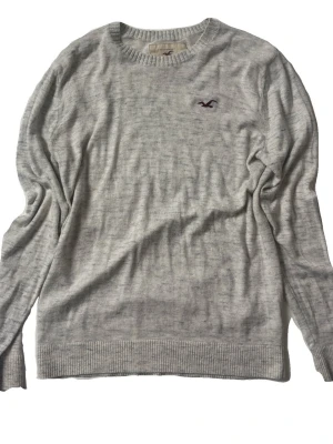 Ljusgrå Hollister tröja - Ljusgrå långärmad tröja från Hollister med rund halsringning och broderad logga på bröstet.