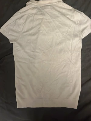 Vit pikétröja från pull bear  - Klassisk vit pikétröja från pull bear med korta ärmar och krage med knappar. Tillverkad i mjuk bomull som känns skön mot huden. Perfekt till en avslappnad och stilren look.