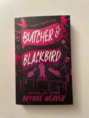 Butcher & Blackbird av Brynne Weaver - En pocketbok med svart och lila omslag, titeln 'Butcher & Blackbird' av Brynne Weaver. Omslaget har grafiska illustrationer av fåglar, motorsåg och kniv, samt siluetter av två personer. Boken blandar romantik och mörk spänning med teman som seriemördare och vänskap.