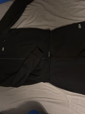 Svarta mjukisbyxor från Lacoste - Säljer ett par svarta mjukisbyxor från Lacoste i slim fit-modell. Byxorna har dragsko i midjan och en liten broderad Lacoste-logga framtill. Perfekta för chill dagar och riktigt sköna att ha på sig. Byxorna är i ny skick och säljs även för halva priset av vad de egentligen kostar på Zalando!