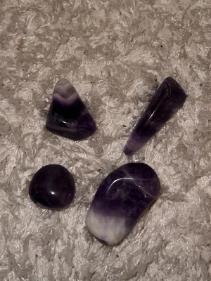 Polerade ametiststenar - Fyra polerade ametiststenar i olika former och storlekar. Stenarna har en djup lila färg med inslag av vitt och svart, vilket ger dem ett unikt och snyggt utseende. Perfekta som dekoration eller för att använda i smyckestillverkning.