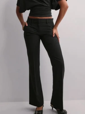 Svarta kostymbyxor med raka ben - Snygga svarta kostymbyxor med raka ben och pressveck. Byxorna har hällor för skärp, fickor fram och fuskfickor bak. Perfekta för en clean och stilren look. Materialet ser ut att vara en mjuk och följsam mix, troligen polyester eller viskos.