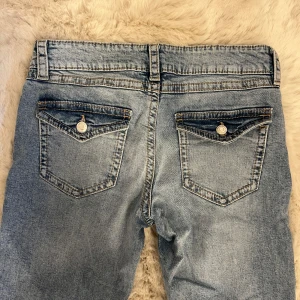 Blå jeans från Gina Young  - Snygga ljusblå jeans från Gina Young med raka ben och lite utsvängda nedtill. Jeansen har silverfärgade knappar och detaljerade sömmar. Materialet är slitstarkt denim i bomull. Aldrig använda!