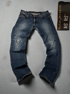 Nudie Jeans Tight Long John 32/32 - Säljer ett par blå slitna jeans från Nudie Jeans, modellen Tight Long John. Jeansen har skinny fit, slitningar och hål på knäna samt klassiska fem fickor. Materialet är 98% bomull och 2% elastan för extra stretch och komfort.