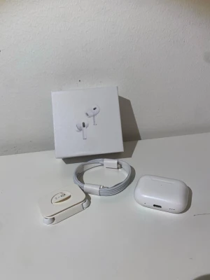 Apple AirPods Pro 2 - Säljer ett par Apple AirPods Pro i vitt med trådlöst laddningsetui. Hörlurarna har en stilren och kompakt design, levereras med originalförpackning, laddningskabel och extra öronproppar. Perfekt för dig som vill ha grymt ljud och smidig anslutning till din iPhone