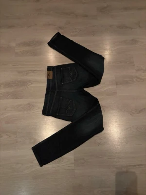 Mörkblå jeans från Replay - Säljer ett par mörkblå jeans från Replay med klassisk femficksdesign och snygga kontrastsömmar på bakfickorna. Jeansen har en rak passform och är tillverkade i slitstark denim med Replay-lapp bak i midjan.