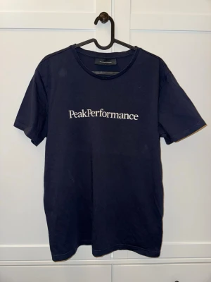 Mörkblå Peak Performance t-shirt - Snygg mörkblå t-shirt från Peak Performance med vit logga tryckt på bröstet. Klassisk rund halsringning och korta ärmar.