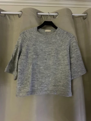 Ljusgrå stickad kortärmad tröja - Mysig ljusgrå stickad tröja med korta ärmar och rund hals. Har en lös tråd på framsidan!🩷