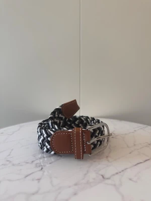 Svart grå vitt flätat bälte - Tja säljer helt nytt klassiskt svenskt flätat bälte från Bältgallerian i storlek 105cm i längd och 3,5cm i bredd. Dem är i ett elastiskt material och finns i flera olika färger i min profil.