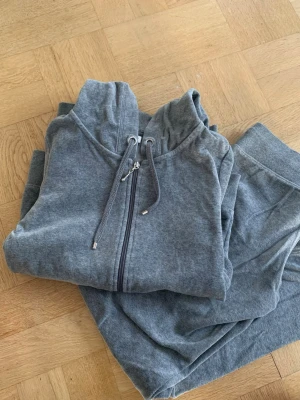 Grått mjukisset med hoodie 🩶 - Säljer ett grått mjukisset med zip-hoodie och matchande byxor. Hoodien har dragkedja, fickor och dragsko i huvan. Byxorna har resår i midjan och dragsko för skön passform. Perfekt för chill hemma eller när du vill vara bekväm.