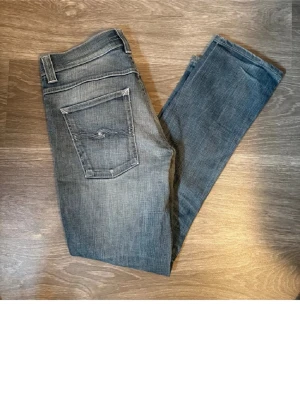 Blå jeans från Nudie Jeans Co - Säljer ett par klassiska blå jeans från Nudie Jeans Co med fem fickor och snygg slitning framtill. Jeansen har rak passform och normal midja. Materialet är mjukt denim i bomull och färgen är tvättad blå med ljusare partier.