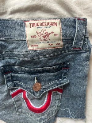 True Religion jeansshorts - Säljer ett par blå jeansshorts från True Religion med ikoniska bakfickor. Använda 1 gång så är så gott som nya. I storlek 26. Nypris 1000 men säljer för 500