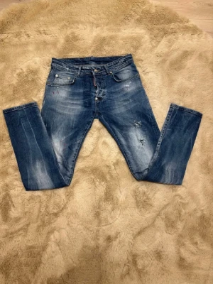 Blå Disquared 2 jeans  - Säljer ett par blå jeans med smal passform och slitna detaljer. Jeansen har fem fickor, knappgylf och coola slitningar samt ljusa tvättade partier. Perfekta för en avslappnad streetstil. Materialet är klassisk denim.Kom dm för eventuella frågor 🧐pris kan alltid diskuteras 😊passar folk mellan 165-180 slim fit