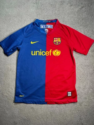 FC Barcelona matchtröja Nike - Säljer en FC Barcelona UNICEF half-and-half retrotröja Nike – Storlek M junior (140-152 cm) Ikonisk 2008/09-jubileumströja – halva blå, halva röd. Samma säsong som trippeln! Äkta Nike, UNICEF-sponsor, broderat emblem, “més que un club”-hals. Fint begagnat skick – inga hål/fläckar, lite noppor men snygg. Perfekt för fans, samlare eller streetwear.  Fråga om mer bilder.  Du som har lillsyskon eller barn som älskar FCB köp till dem! 