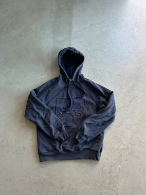 Fet Cohen hoodie - Säljer en mörkblå hoodie från J.Cohen med broderad logga och stiliserad blomdesign på bröstet. Hoodien har en klassisk huva med dragsko och ribbade muddar vid ärmslut och nederkant. Perfekt för dig som gillar stilrena detaljer. Pris inte hugget i sten!