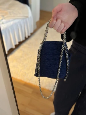 Mörkblå virkad axelväska med kedja - Snygg mörkblå axelväska som är i virkat material med en lång silverfärgad kedjerem. Väskan har en fyrkantig form och är perfekt för att bära det viktigaste. Enkel men trendig design som passar till många outfits.