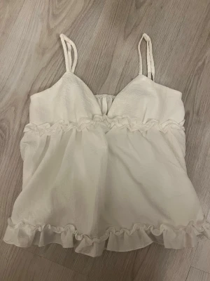 Krämvit linnetopp med volang - Söt krämvit linnetopp med tunna axelband och volangdetaljer både upptill och nedtill. Pris kan alltid diskuteras 💕