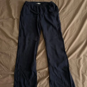 Mörkblå linnebyxor - Snygga mörkblå linnebyxor från Ryvals Stockholm. Byxorna har raka ben och är tillverkade i ett lätt och luftigt linnematerial. Det finns fickor på framsidan men inte på baksidan. Snöret i midjan är försvunnet men de funkar lika bra ändå och är inget som man tänker på. Byxorna är i bra skick och bara använda ett par gånger.