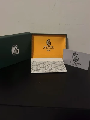 Vit korthållare från Goy4ard - Snygg vit korthållare från Goy4ard med det klassiska mönstret i grått och svart. Tillverkad i exklusivt läder och har flera fack för kort. Kommer med originalask och certifikat. Perfekt accessoar för dig som gillar stilrena detaljer.