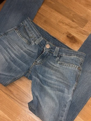Blå lågmidjade jeans - Säljer ett par blåa lågmidjade jeans med snygga detaljer på bakfickorna. Dom är lite mer raka än utsvängda. Dom är i jättebra sick, nästan aldrig använda. Jättefint för nån som gillar en avslappnad stil.