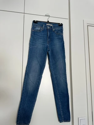 Blå raka jeans från Levi's - Säljer ett par klassiska blå jeans från Levi's med rak passform och hög midja. Jeansen har fem fickor, snygga slitningar och Levi's ikoniska läderpatch bak i midjan. Perfekta till sneakers eller boots för en avslappnad look. Jeansen har vissa slitningar tex som sträck höger baksida. 