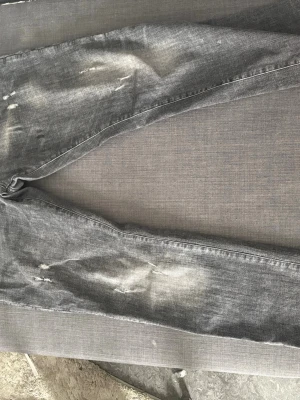 Grå slitna jeans med patch - Säljer ett par grå jeans från Philipp Plein med slitningar och distressed detaljer. Jeansen har raka ben och en patch på ena bakfickan. Klassisk femficksmodell i denim med cool tvätt och råa kanter.