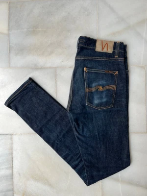 Mörkblå jeans från Nudie Jeans - Ett par riktigt snygga jeans ifrån Nudie Jeans med snygg slitning på bakfickan ———————————————————————————-                                                                        📐| Storlek: 31-34                                                   👖| Märke: Nudie Jeans                                         🔎 | Skick: Mycket bra                                            💵 | Ny Pris: 1599kr                                                 ✍🏻 | Skriv om du har några frågor