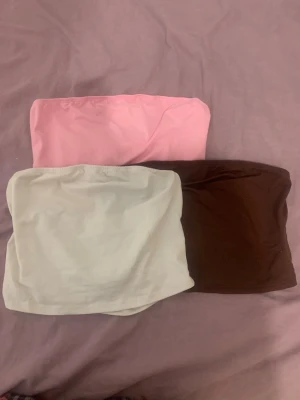 3-pack bandeau tubtoppar i pastell - Säljer ett 3-pack bandeau tubtoppar i rosa, vit och brun. Perfekta att styla till jeans eller kjol för en enkel och trendig look. Alla toppar är ärmlösa och har en mjuk, stretchig passform.