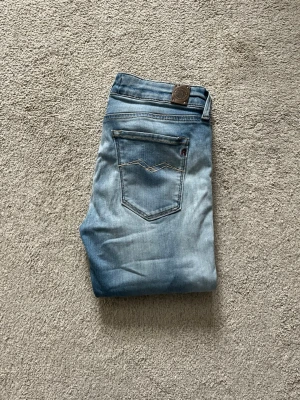 Ljusblå jeans från Replay Luz - Säljer ett par ljusblå jeans från Replay Jeans med klassisk femficksdesign och snygga kontrastsömmar. Jeansen har en avslappnad passform och är tillverkade i mjuk denim. Perfekta för en casual look!