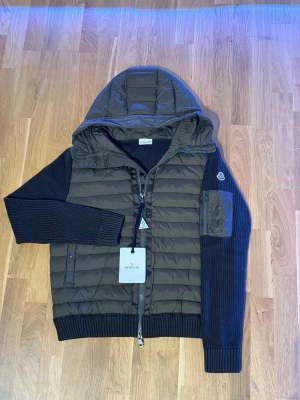 Grön Moncler cardigan med huva - Snygg mörkblå pufferjacka från Moncler med stickade ärmar och quiltad front. Det står att den är i storlek xxl men den sitter som en M . Den är helt ny med lappen och allt kvar på den. 
