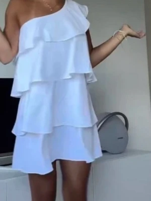 Vit volangklänning med axelbandslös design - Säljer nu min konfa/sommar klänning. Snygg vit kortklänning med flera volanger och smala axelband. Klänningen har en luftig passform och är perfekt för varma dagar. Enkel och stilren design som känns fräsch och modern. Hör av er för fler bilder 