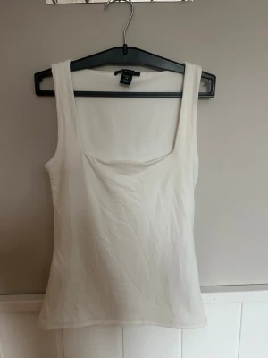 Vit topp från Amisu - Säljer en enkel och stilren vit linnetopp från Amisu. Toppen har breda axelband och en rak, något figurnära passform. Perfekt att matcha med jeans eller kjol för en clean look.