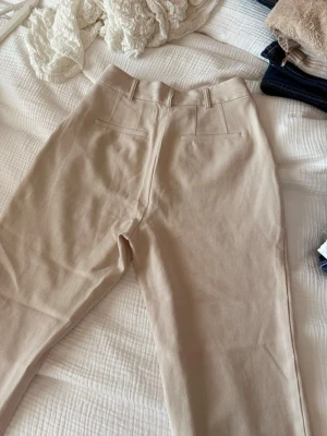 Beige kostymbyxa med hög midja - Snygga beige kostymbyxor med hög midja och raka ben. Köpta för många år sen på NA-KD. En knapp fattas på insidan men ingenting som syns eller påverkar passformen. 
