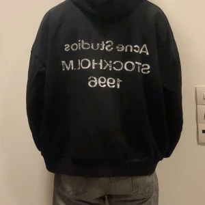 Svart hoodie Acne Studios - Säljer en svart hoodie från Acne Studios med stor vit text på ryggen: 'Acne Studios STOCKHOLM 1996'. Klassisk passform med huva och ribbade muddar. Perfekt för dig som gillar streetwear och vill ha något från ett ikoniskt svenskt märke. Säljer den då jag tyckte att den var för baggy och är inte min stil. Så säljer då jag har haft liggandes i ett tag och inte kunnat använda den. Storlek M. Två parfymer följer med!