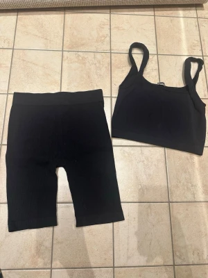 Svart ribbat set från Zara - Säljer ett svart ribbat set från Zara med crop top och cykelbyxor. Setet har breda axelband och hög midja på byxorna. Materialet är stretchigt och följsamt, perfekt för en sportig look eller chill dagar.