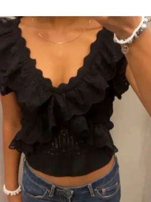 Svart volangtopp från Zara - Supersnygg svart topp från Zara med djup v-ringning och volangdetaljer framtill. Croppad modell som passar perfekt till höga jeans eller kjol. Tunn och luftig, perfekt för varmare dagar.