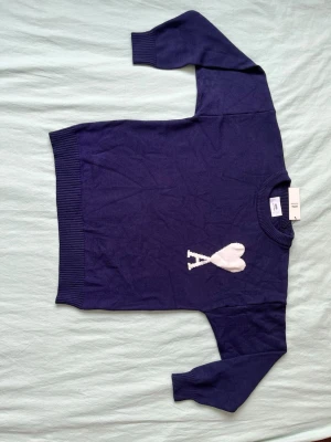 Mörkblå stickad tröja från Ami - Mörkblå stickad tröja från Ami med rund halsringning och ribbade muddar. På bröstet finns ett vitt hjärta med bokstaven A. Perfekt för dig som gillar stilrena detaljer och vill ha något som sticker ut.