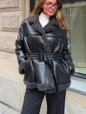 Svart skinnjacka med bälte - Skinnjacka i läderimitation med teddyfoder. Jackan är svart och har oversize fit. Den har midjebälte i midjan med spänne, fickor i sidorna och långa ärmar med fuskpäls vid ärmsluten. Helfodrad.