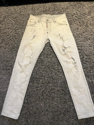 Ljusgråa distressed jeans från Dsquared2 - Säljer ett par ljusgråa jeans från Dsquared2 med slitningar och distressed detaljer på både fram- och baksidan. Jeansen har smal passform, klassiska fem fickor och är tillverkade i denim. Perfekt för dig som gillar en edgy och trendig look.