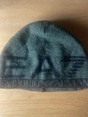 Svart mössa från EA7 Emporio Armani - Säljer en svart mössa från EA7 Emporio Armani med klassisk logotyp på insidan. Mössan är enkel och stilren, perfekt för dig som vill ha ett snyggt accessoar till hösten och vintern. Materialet känns mjukt och bekvämt.
