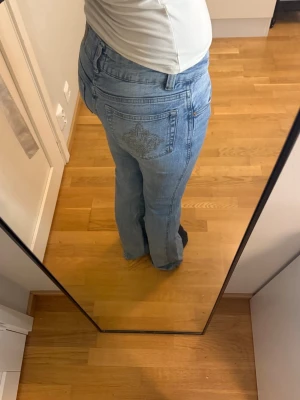 Ljusblå bootcut jeans med brodyr - Hej finisar!💕 Säljer ett par ljusblå bootcut jeans med snygg broderad detalj på bakfickan. Klassisk femficksmodell med knapp åt sidan och dragkedja framtill. Jeansen har en avslappnad passform och är perfekta för en chill och trendig look. Skriv om ni är intresserade!!🌸