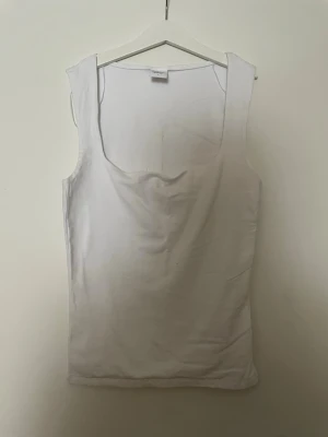 Vit linnetopp från Gina Tricot - Säljer en enkel och stilren vit linnetopp från Gina Tricot. Toppen har breda axelband, fyrkantig ringning och ärmlös design. Perfekt att matcha med jeans eller kjol för en clean look.